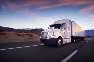 White semi truck on the highway at sunset with mountains in the background