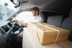Delivery driver man driving a sprinter van that has boxes and parcels on seat outside of a warehouse